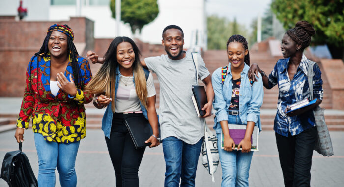 Group of five african college students spending time together on campus at university yard. Black afro friends studying. Education theme.